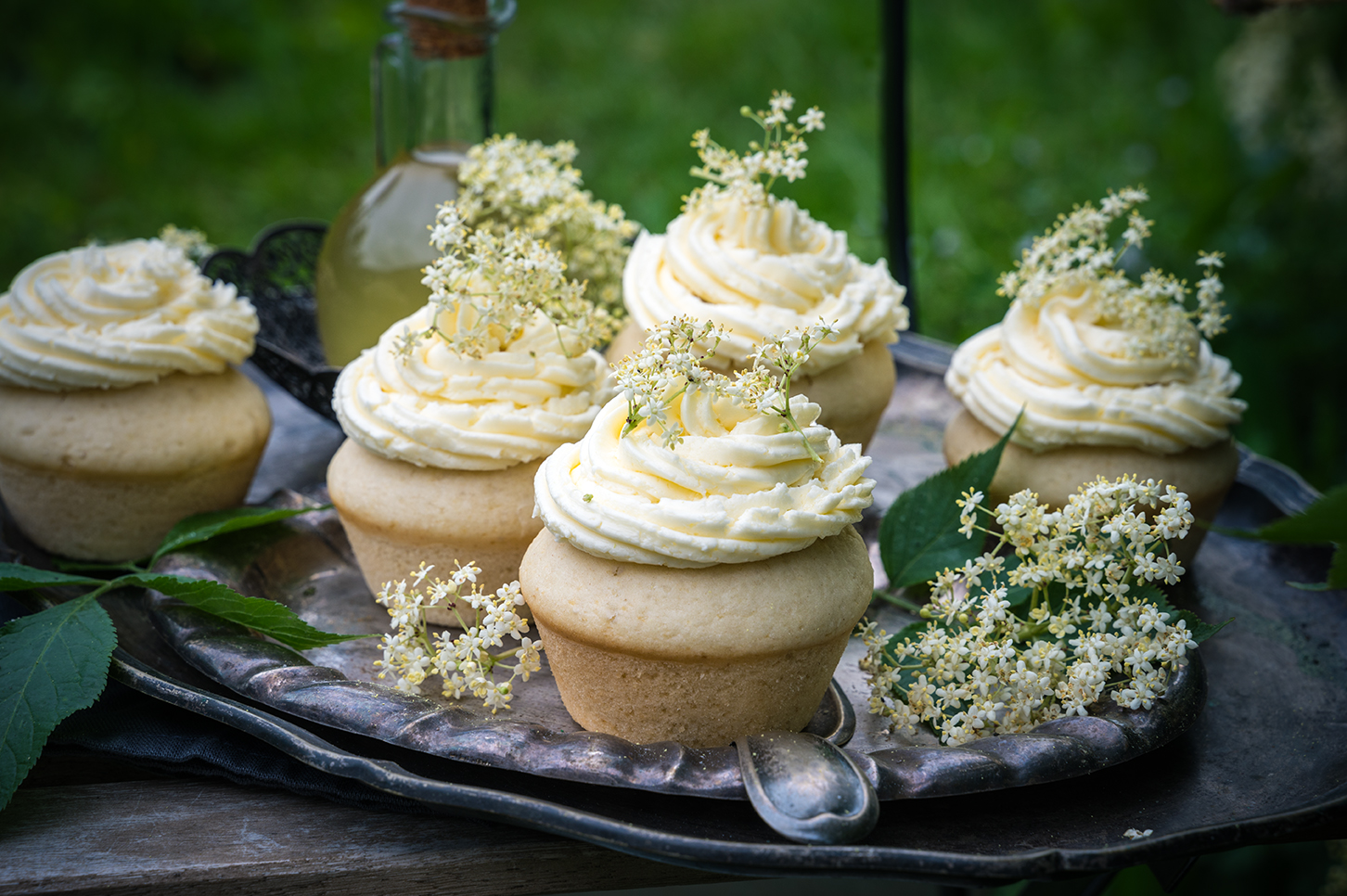 Vegane Zitronen-Cupcakes mit Holunderblüten Creme stehen auf einem Silbertablett im Garten.